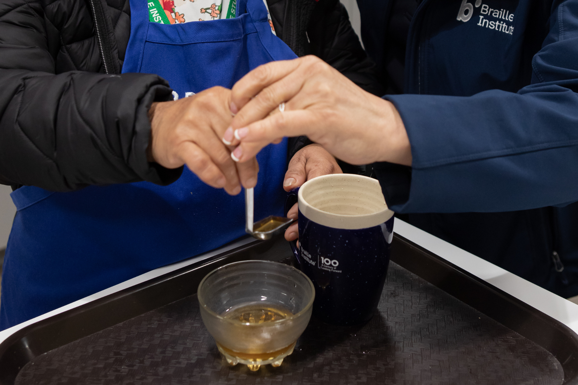 Primer plano de un instructor que ayuda a un estudiante a medir líquido para verterlo en una taza.
