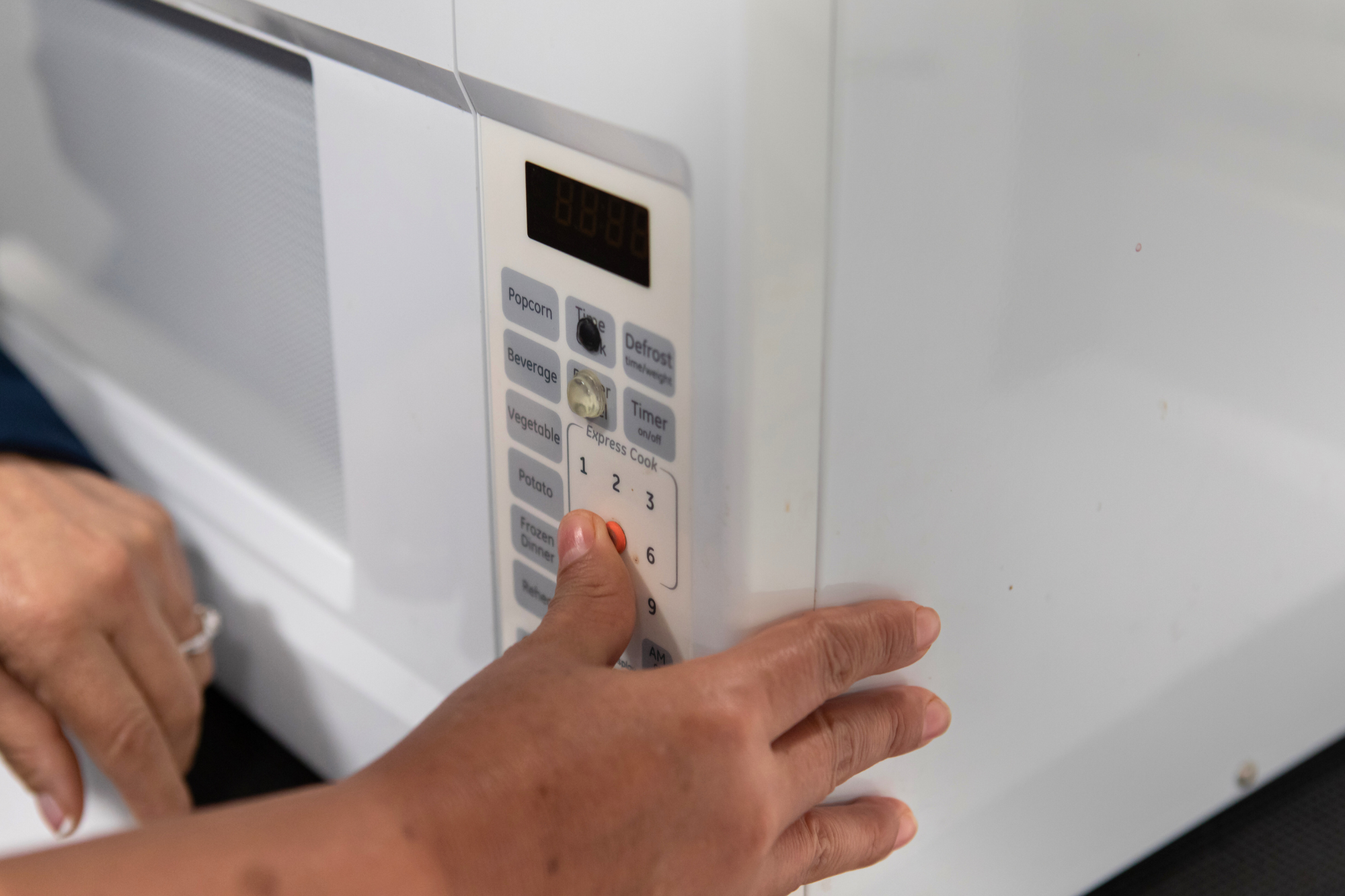 Close-up of a student's hand on a microwave, their thumb over a bright orange bump dot over the 5 minute button.