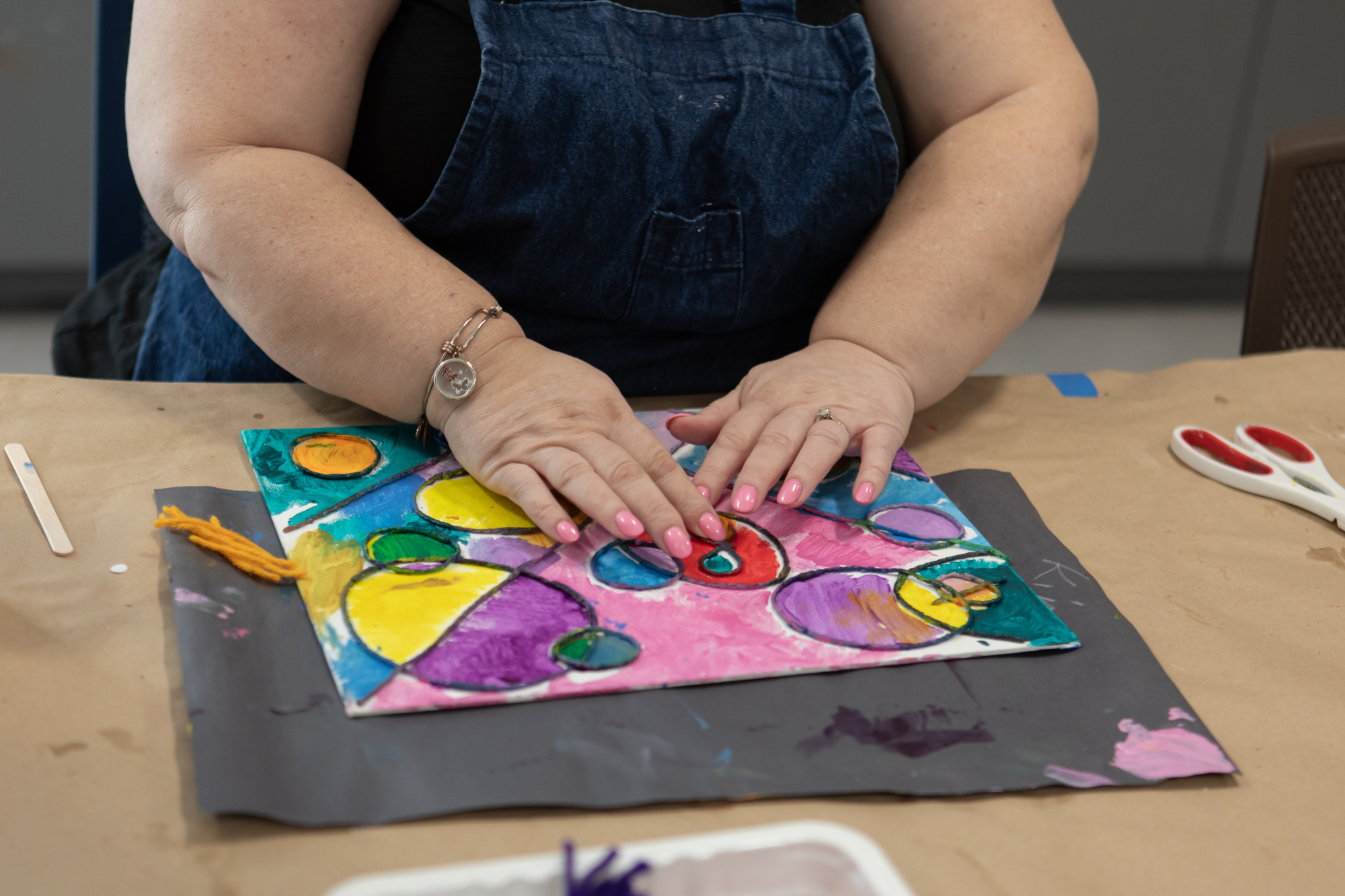 Close-up of a student's hands over her colorful tactile painting. Her pink nails match the bright pink featured in the center of her piece.