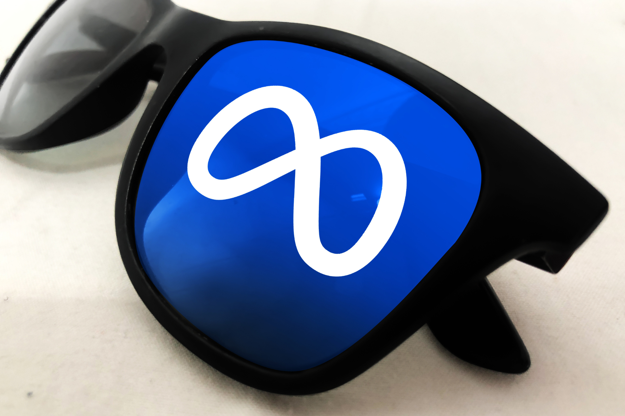 Close-up photo of a pair of black glasses frames. One lens is edited to be bright blue with the Meta logo.