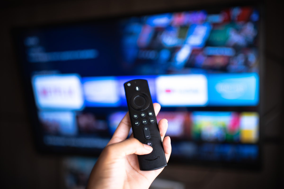 Person holding Fire TV remote in front of television screen.